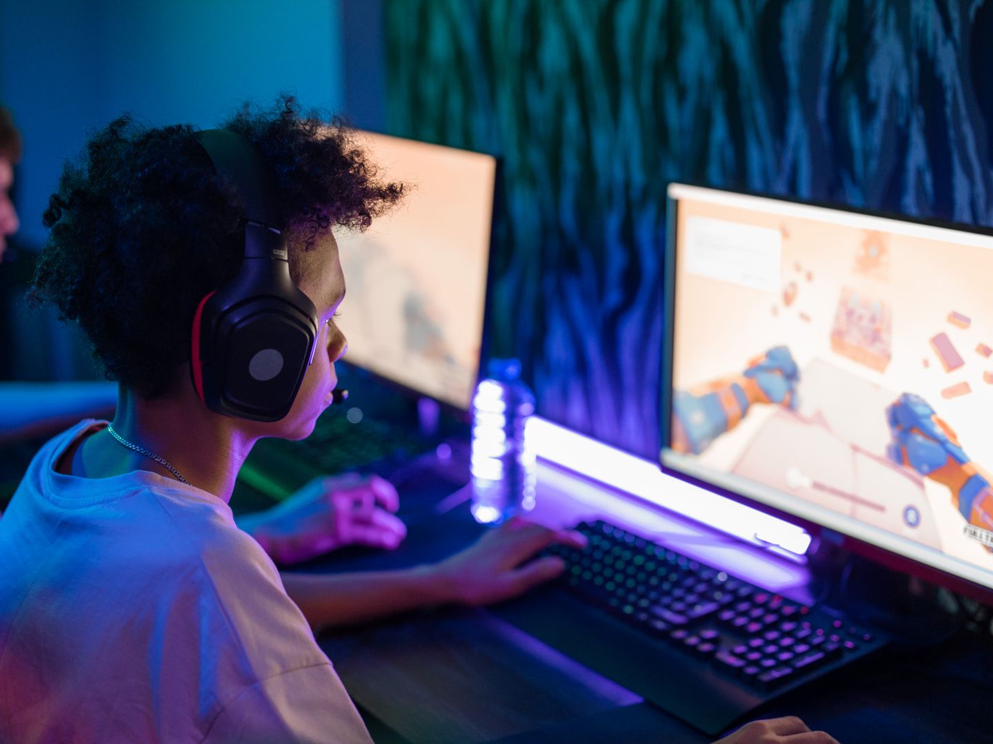 Teen gamers engrossed in online computer game in a vibrant, modern gaming room.