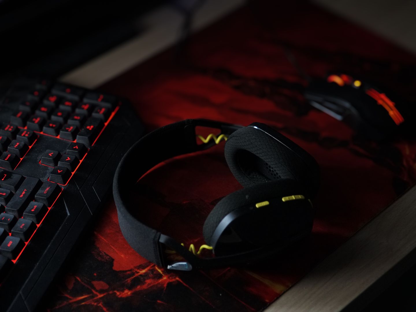 A sleek gaming setup featuring a backlit keyboard, wireless headphones, and a gaming mouse on a vibrant desk pad.